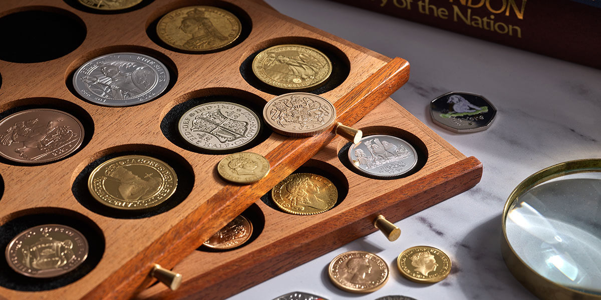 A photograph of a historic coin collection in protective drawers with a magnifying glass and coin reference book on the edge of the shot.