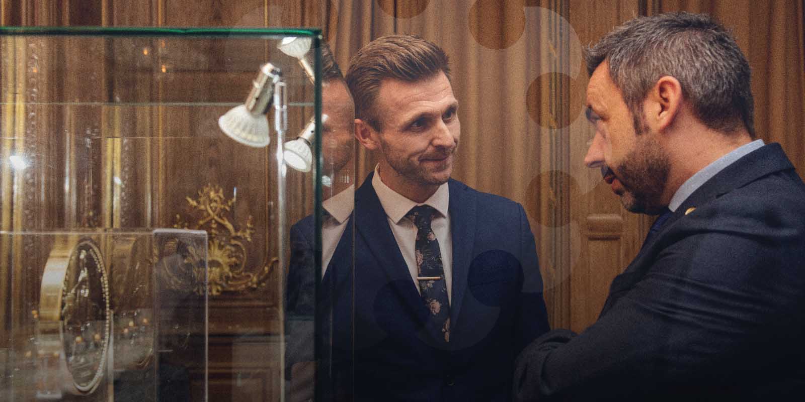 Two men in business attire talking in front of a display case containing a huge gold coin.